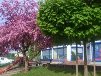 Eine Außenansicht der Kita Niederscheld mit rosa blühenden Bäumen