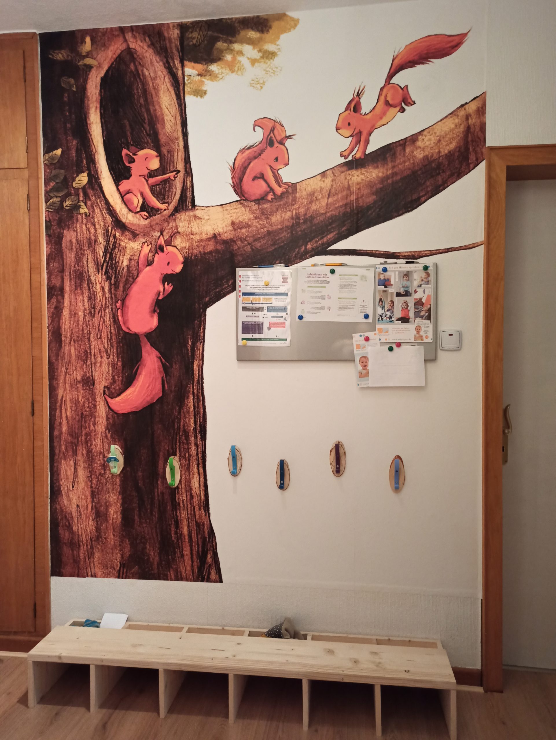 Die Garderobe für die Tageskinder. Eine lustige Fototapete in diesem Bereich zeigt Eichhörnchen, die an einem Baum klettern und über die Äste tollen.